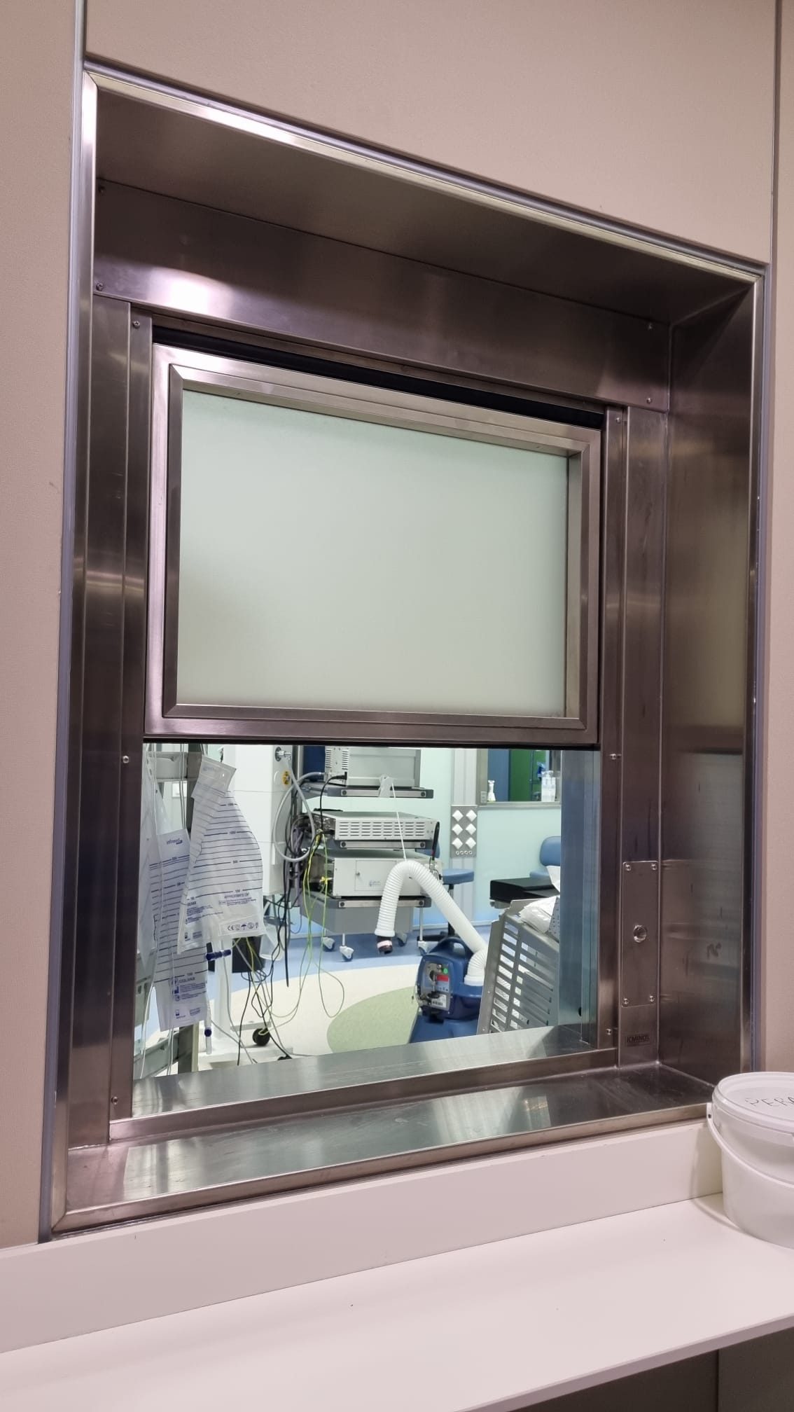 Ventanas guillotina motorizadas VG-24 de acero inoxidable con vidrio emplomado. Máxima seguridad, estanqueidad y control en quirófanos hospitalarios.